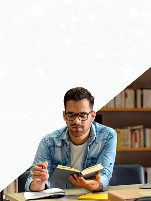 A man in glasses wearing a denim shirt, reading a book.